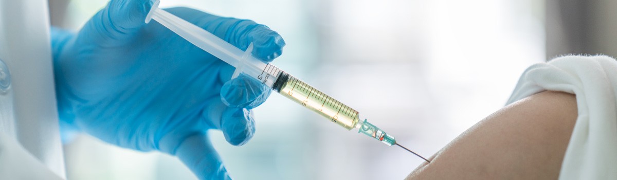 File Photo of Gloved Hand Holding Syringe Up to Arm
